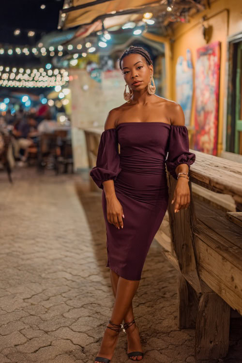 A Black woman in a chic off-the-shoulder plum midi dress with strappy heels and statement earrings, posing outside a lively fall night bar, full body outfit visible