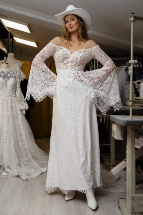 a woman wears white cowboy boots with a wedding dress and a hat