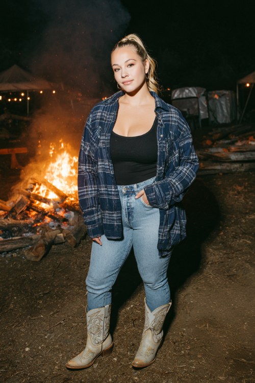 A curvy woman wears skinny jeans with an oversized navy flannel shirt as a jacket, layered over a fitted black tank