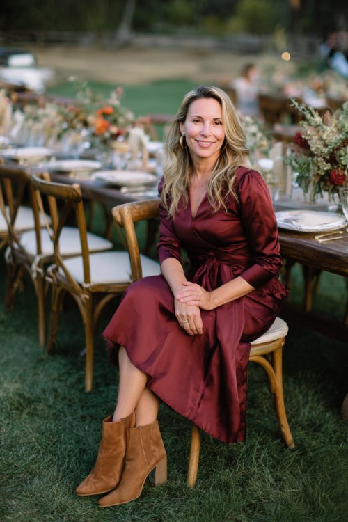 A woman over 50 in a burgundy A-line midi dress with three-quarter sleeves, paired with camel boots