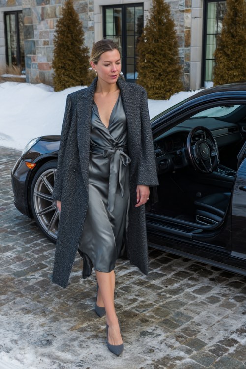 A woman wears a dark gray satin wrap dress with a structured wool coat and pointed heels