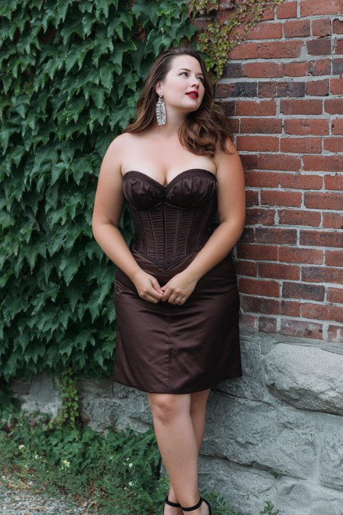 A plus-size woman wears a chocolate-brown cocktail dress with sweetheart neckline, corset-style bodice, and satin skirt (3)