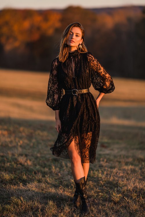 A woman wears a black lace dress with sheer bishop sleeves, paired with ankle boots and a wide leather belt