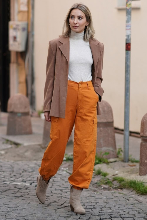 a woman wears cowboy boots with organe cargo pants and beige coat