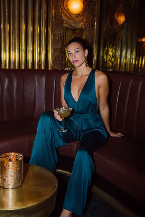 A woman over 30 wears a jewel-toned satin jumpsuit with wide legs and a plunging neckline