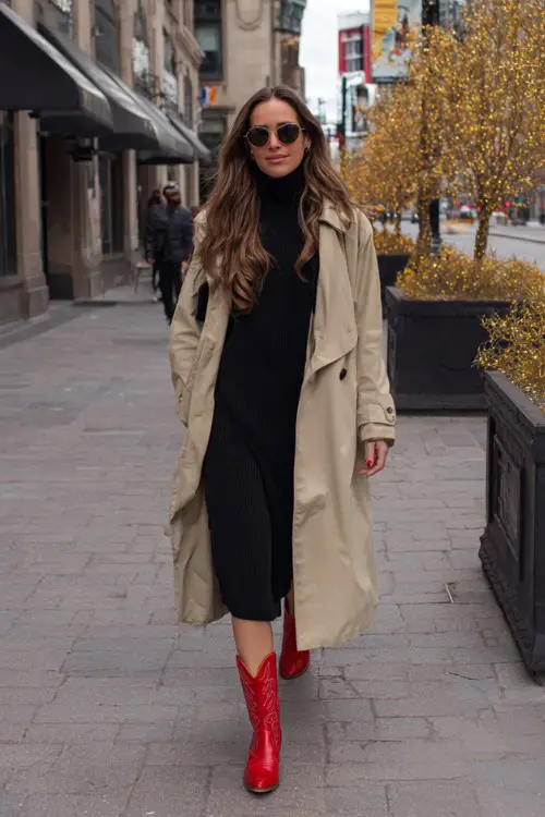 A woman over 30 wears red cowboy boots with a beige trench coat layered over a black turtleneck dress