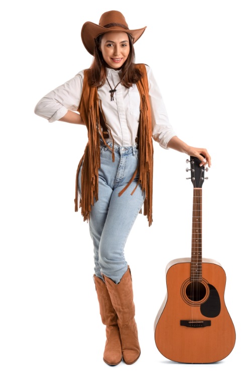 A woman wears brown cowboy boots with jeans, a white shirt and a fringe coat