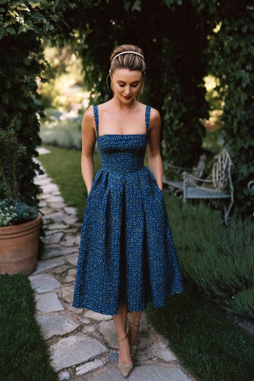 A petite woman wears a midnight navy tea-length A-line with a square neckline and tiny ditsy print, paired with kitten heels and a pearl headband