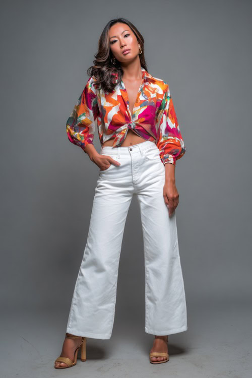 A woman in a bold printed blouse with white wide-leg jeans and platform heels, styled for a stylish summer evening in NYC, simple studio background