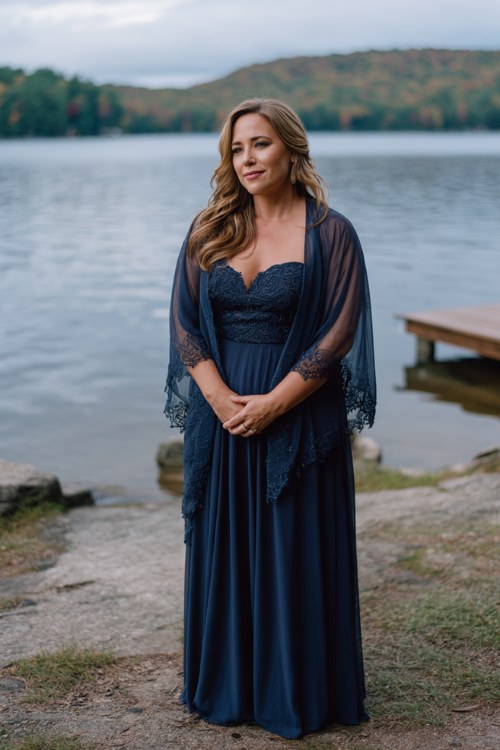 A curvy woman wears a navy chiffon gown with sheer embroidered overlay and a flowy hem