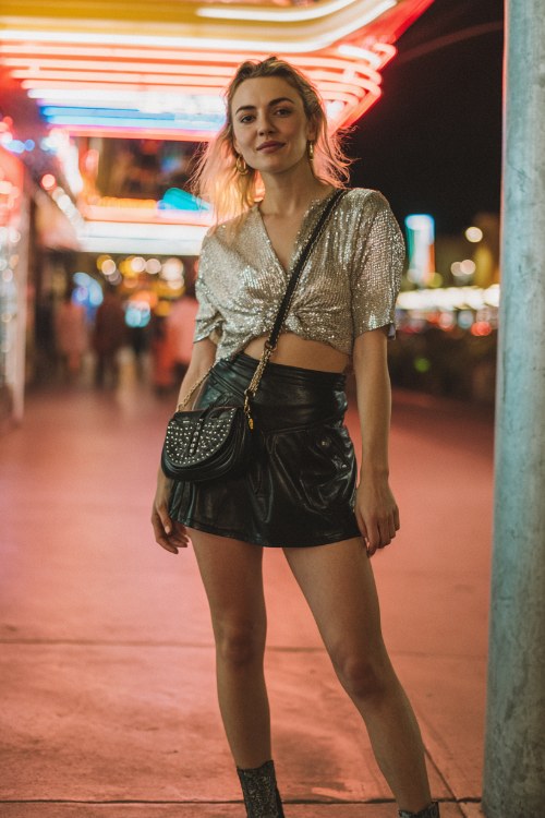 A woman wears a black leather mini skirt paired with a sequined silver crop top