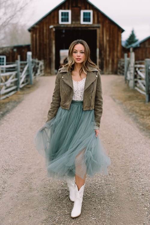 A petite woman in a sage green tulle midi dress with a lace bodice and sheer long sleeves, styled with white cowboy boots