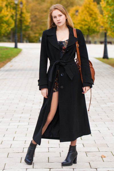 A woman wears black ankle cowboy boots with mini dress, and black long coat