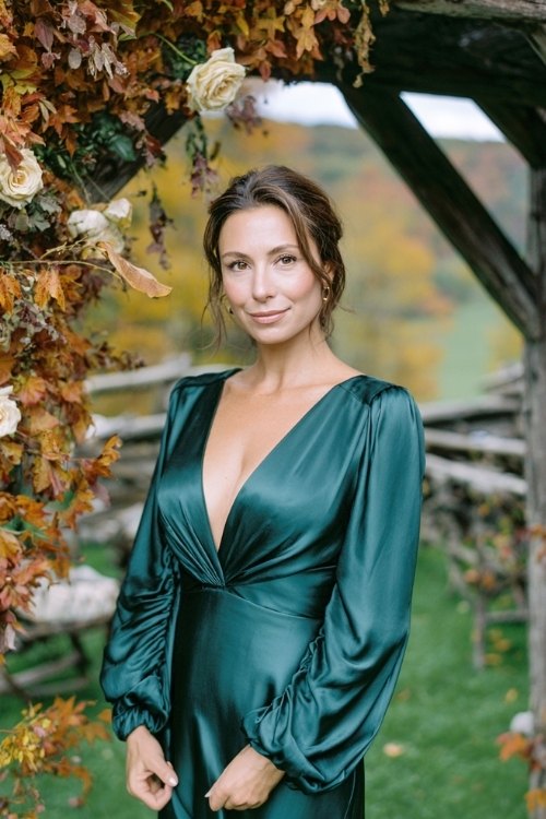 a woman over 50 in a deep emerald satin wrap gown with bishop sleeves, standing beneath a rustic wooden arch