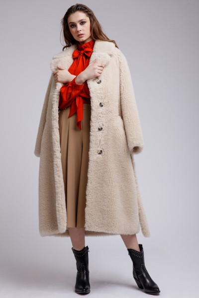 A woman wears trench coat, skirt, red top and cowboy boots