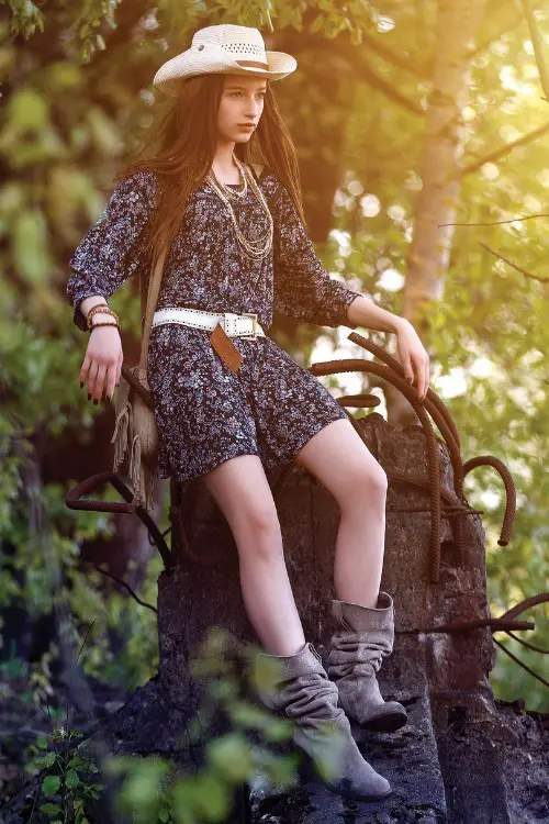A woman wears floral dress with cowboy boots and a cowboy hat
