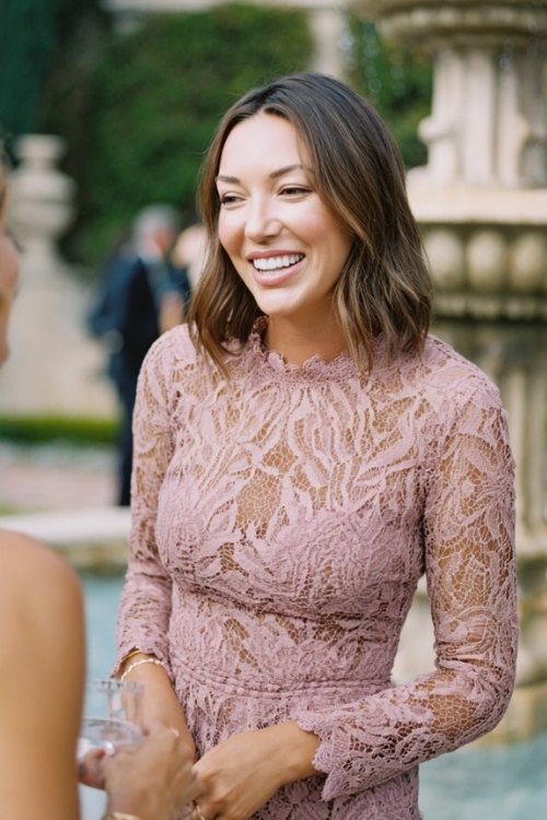 a woman over 50 in a dusty rose lace midi dress with scalloped hem and high neckline