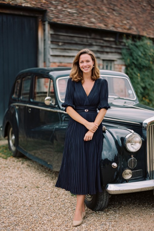 A woman over 50 wears a navy pleated midi dress with elbow-length sleeves and a sash belt