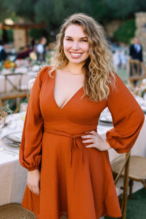A curvy woman in a burnt orange long-sleeve dress with a cinched waist and flared hem