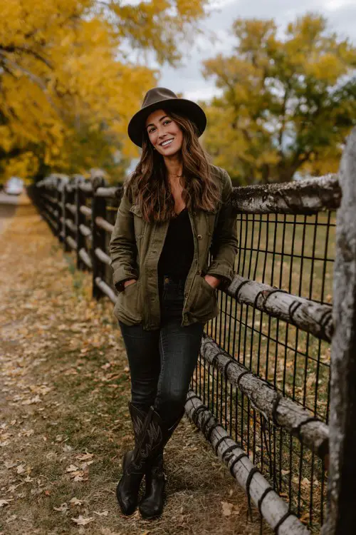 A curvy woman over 30 wears tall black cowboy boots with dark skinny jeans, olive green jacket