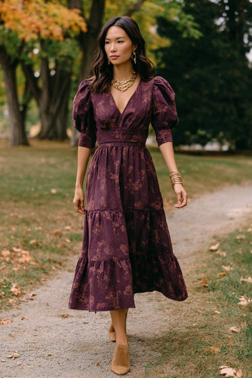 A woman wears a deep plum midi dress with puff sleeves, a tiered skirt, and vintage-inspired floral patterns, styled with camel suede mules