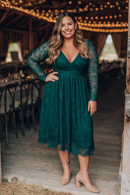 A plus-size woman wears a forest green long-sleeve lace midi dress with a fitted bodice and flowy skirt, styled with beige block heels