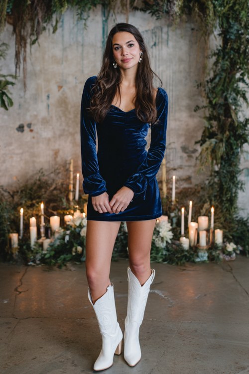 A woman wears a navy velvet sheath dress with long sleeves, styled with white cowboy boots (2)