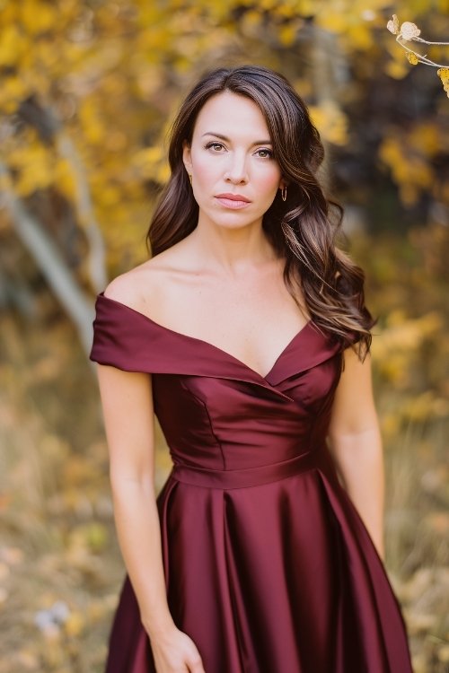 a woman in a deep burgundy satin gown with a flowy skirt and off-shoulder neckline