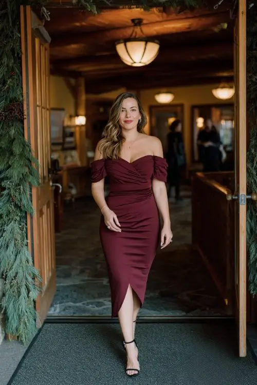 A curvy woman wears a burgundy off-the-shoulder midi dress with soft pleats and heels