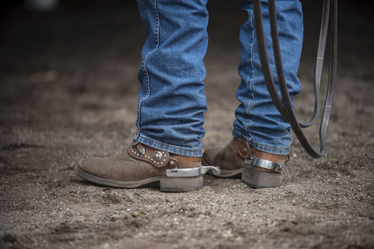 A man wears jeans with cowboy boots on the ranch.