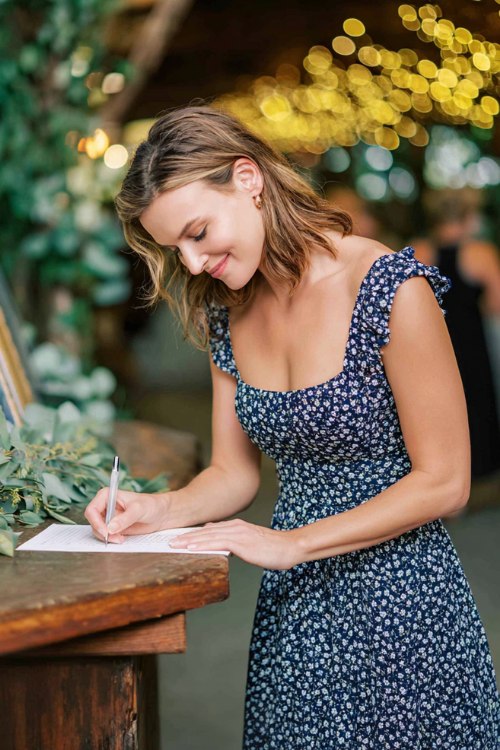 A petite woman wears a navy micro-floral tea-length dress with a square neckline and smocked back