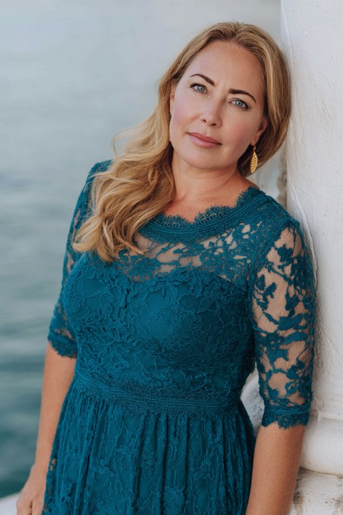 A curvy woman over 50 wears a teal lace A-line dress with 3_4 sleeves and scalloped edges
