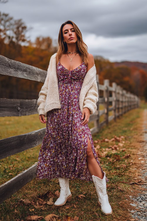 A woman in a floral maxi dress styled with a chunky knit cardigan and white cowboy boots