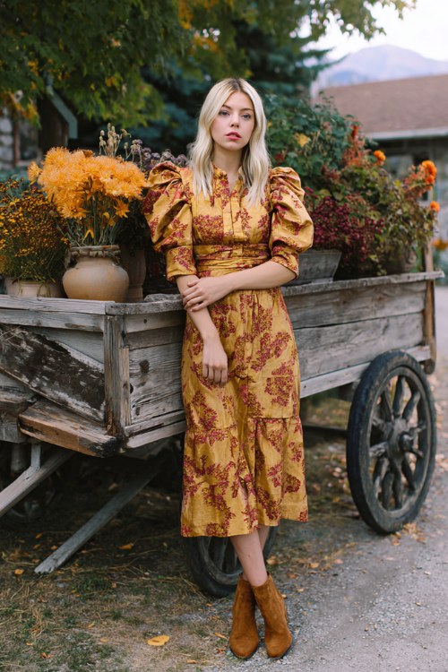 A woman over 30 wears a patterned jacquard midi dress in golden hues with puff sleeves, paired with brown suede heels