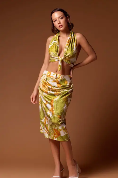 A woman wearing a silky two-piece set with a tie-front crop top and matching midi skirt, styled with wedge heels for a trendy summer bar look
