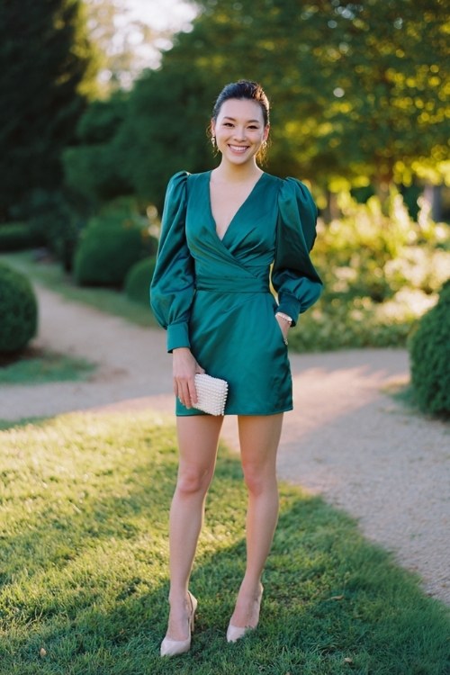 A woman wears a short satin wrap dress in emerald green with puff sleeves (3)