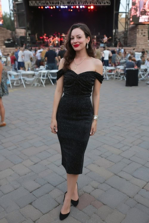 A woman wears a chic black off-shoulder midi dress with subtle shimmer, paired with kitten heels