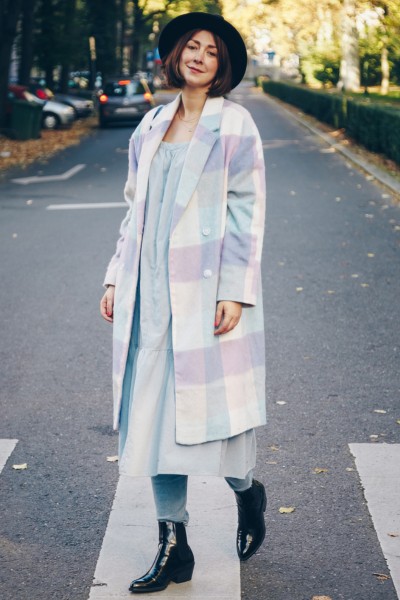 A woman wears black boots, jeans, dress and coat