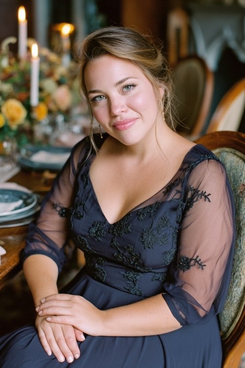 a plus size woman in a navy A-line dress with sheer sleeves and floral embroidery, seated on a vintage chair