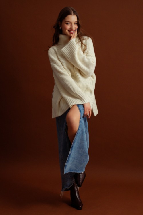 A woman wears brown cowboy boots with a sweater and a denim skirt