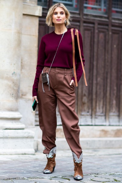 A woman wears brown pants, cowboy boots and dark red sweater