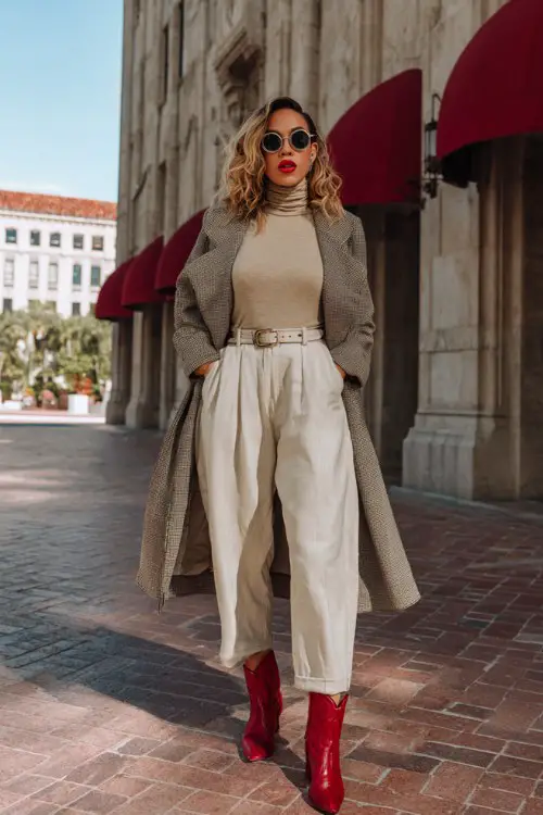 A curvy woman wears red cowboy boots with wide-leg trousers, a beige turtleneck, and a belted wool coat
