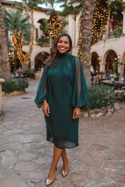A curvy woman over 40 wears a dark green high-neck chiffon dress with flowy sleeves and gold pumps