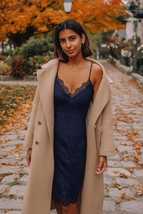A woman in a navy slip dress with lace trim and a light camel wool coat draped over her shoulders