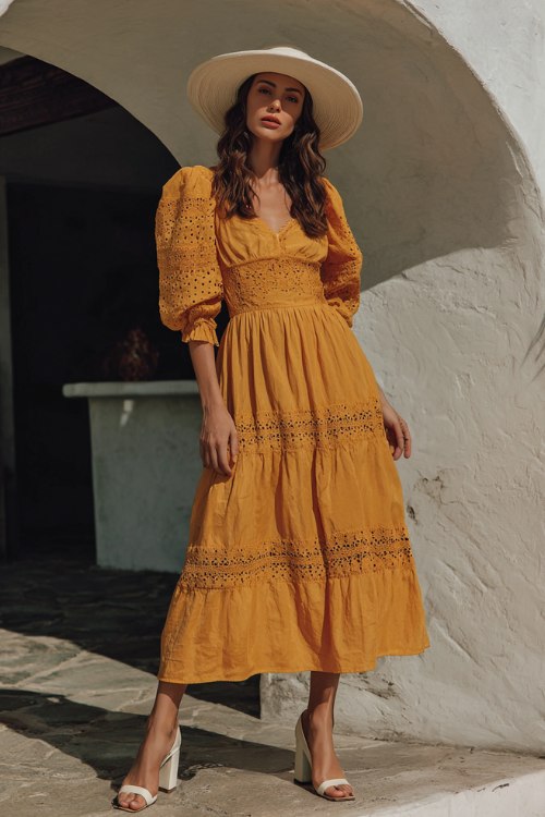 A petite woman wears a mustard yellow boho cocktail dress with puff sleeves, lace cutouts