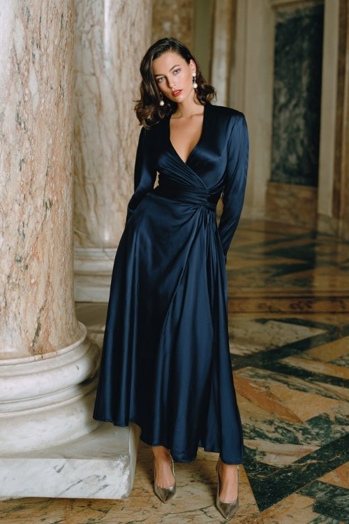 A woman over 40 wears a navy satin A-line gown with a draped bodice and long sleeves