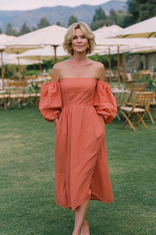 A woman over 50 wears a coral off-the-shoulder midi dress with puff sleeves and a flowy chiffon skirt