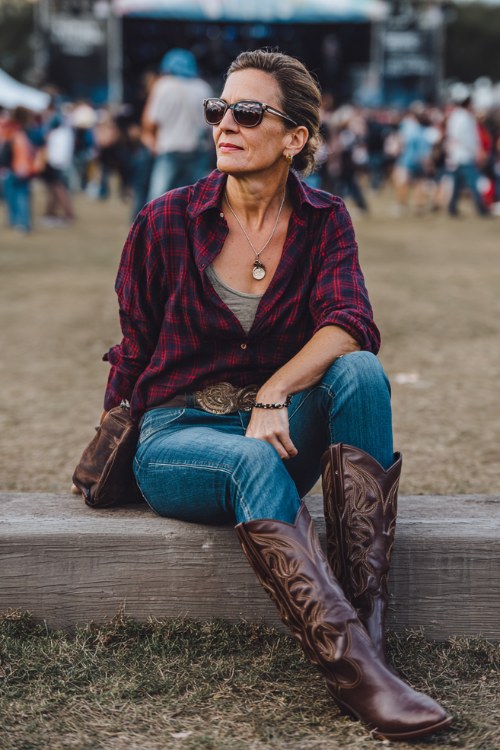A woman over 40 wears classic indigo jeans with a deep red flannel tucked in, styled with sleek brown cowboy boots and a leather belt