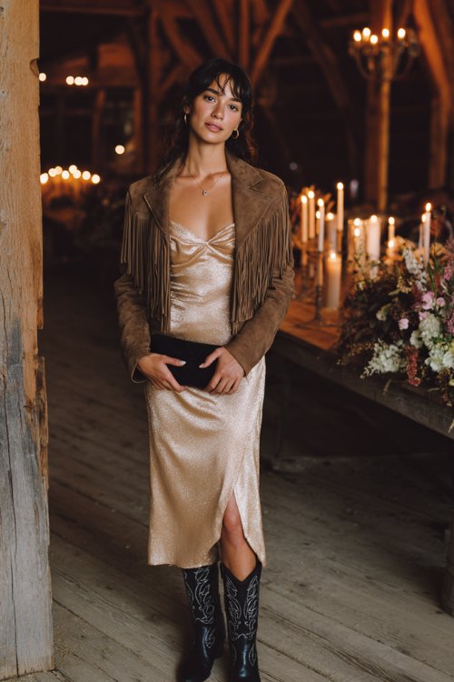 A champagne sequin slip dress layered under a cropped fringed suede jacket, paired with black embroidered cowboy boots
