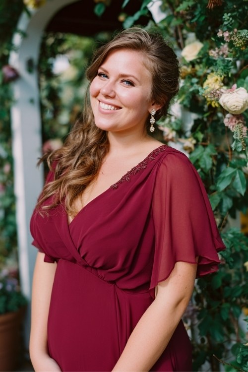 A plus size woman wears a wine-colored chiffon gown with flutter sleeves, accessorized with delicate earrings